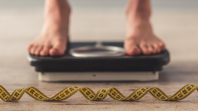 Un ruban à mesurer et derrière un pèse-personne avec quelqu'un dessus. On ne voit que ses pieds.