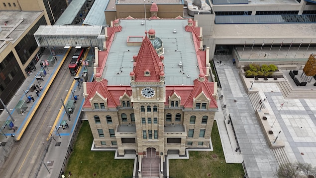 Plan aérien d'un bâtiment beige avec une tour et une toîture rouge. Horloge au centre de la tour. Mai 2026.