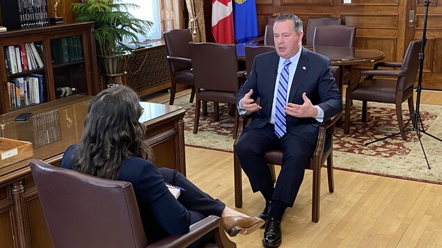 Le premier ministre de l'Alberta assis dans son bureau en face d'une journaliste accordant une entrevue.