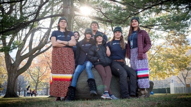 Sept jeunes femmes dont certaines sont assises sur un rocher posent sous l'ombre d'un arbre
