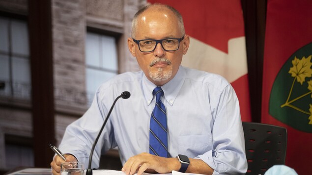 رئيس الخدمات الطبية في أونتاريو، الدكتور كيران مور، متحدثاً في مؤتمر صحفي ويبدو خلفه علما كندا وأونتاريو.