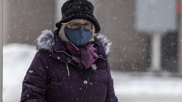 Une femme portant un masque marche dehors pendant qu'il neige.