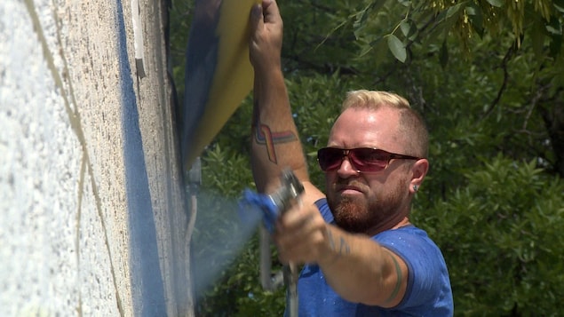 Un homme étend de la peinture sur un mur à l'aide d'un vaporisateur