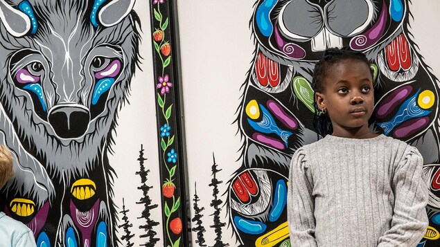 Une jeune fille se tient debout devant une murale illustrant un castor.