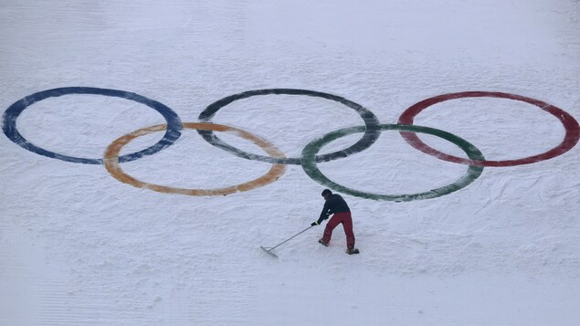 Un employé ratisse la neige devant les anneaux olympiques.