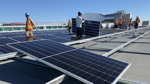 Travailleurs manipulant des panneaux solaires noirs qu'ils installent sur des structures métalliques argentées par une journée ensoleillée.
