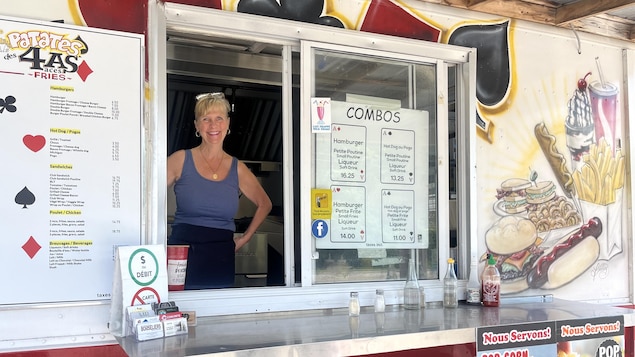 Une femme souriante, debout derrière la fenêtre d'un camion converti en casse-croûte.