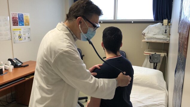 Un médecin portant un masque place le bout de son stétoscope sur le dos d'un patient.