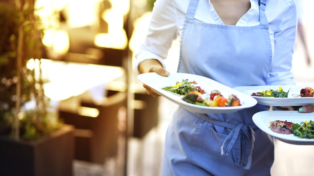 Une serveuse avec plusieurs assiettes remplies dans ses mains dans un restaurant.
