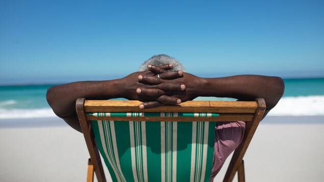 Vue de dos d'un homme assis sur une chaise de plage avec les mains croisées derrière sa tête.