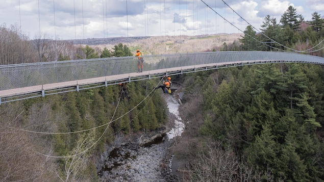 Un ingénieur est accroché sous le pont suspendu, à plusieurs dizaines de mètres de hauteur.