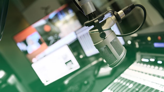 Un micro dans un studio de radio avec des écrans et une console en arrière-plan. 