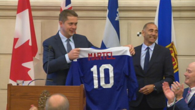 Le nom Martel et le chiffre 10 sont imprimés au dos du chandail bleu que le chef remet au nouveau député devant le caucus. Le nom Martel et le chiffre 10 sont imprimés au dos du chandail bleu que le chef remet au nouveau député devant le caucus.