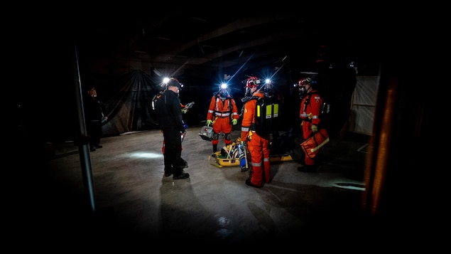Une équipe de sauvetage minier dans une salle sombre devant un évaluateur.