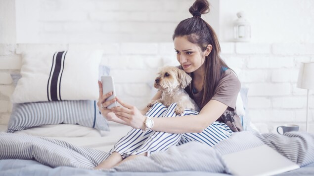 Une femme tient son chien sur elle alors qu'elle prend un égoportrait avec son téléphone intelligent.