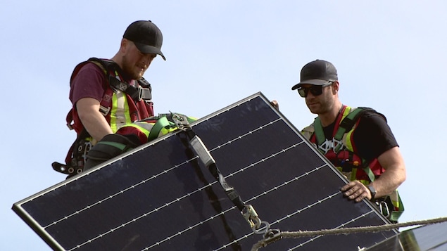 Deux employés tiennent un panneau solaire sur un toit.