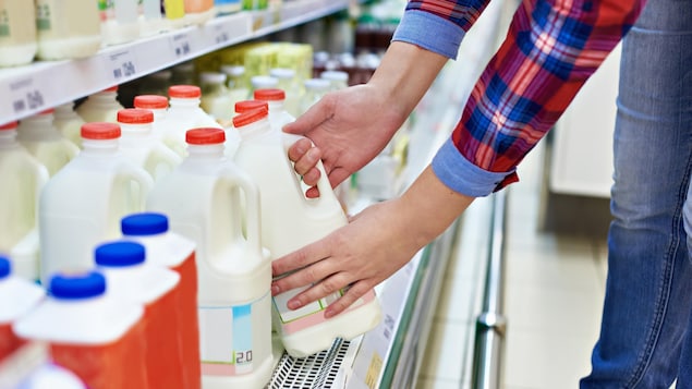 Une femme qui prend une bouteille de lait sur une étagère d'une épicerie.