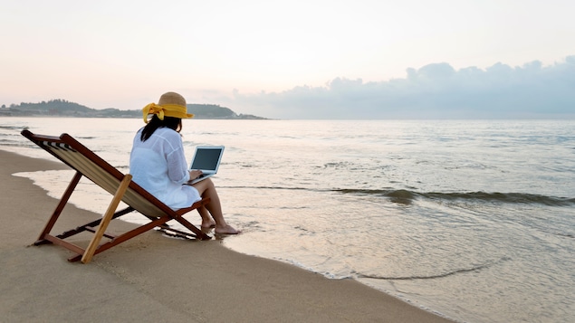 Une femme assise sur une chaise sur le bord d'une plage en train de travailler sur un ordinateur portable.