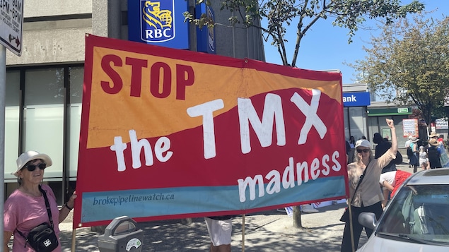 Deux manifestantes tiennent une banderole "Stop the TMX madness" devant la banque RBC.