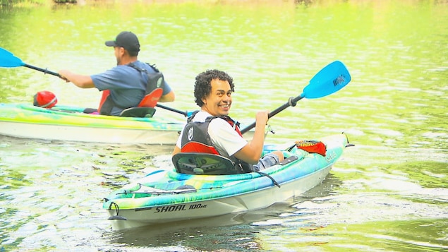 Deux hommes en kayak sur l'eau, dont un qui sourit à la caméra.