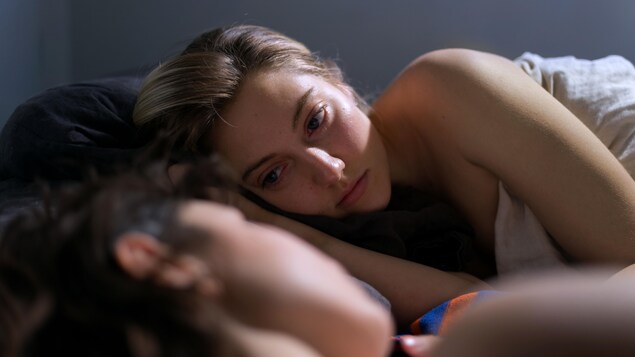 Deux jeunes femmes couchées dans un lit se regardent. 