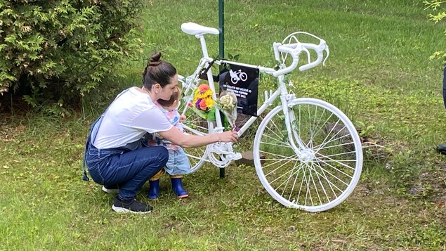 Une femme et sa fillette déposent des fleurs sur un vélo peint en blanc.