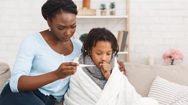 Una madre mirando un termómetro junto a su hijo enfermo.
