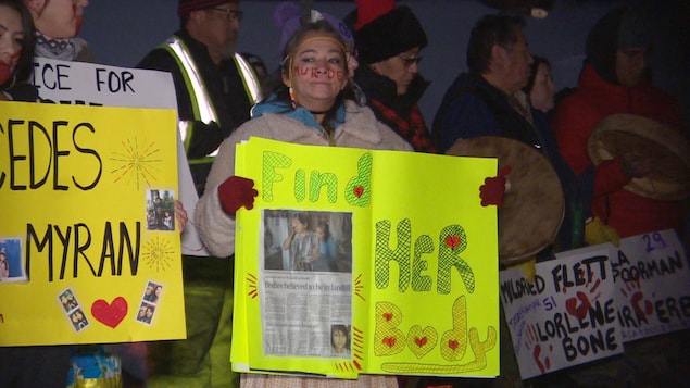 Une femme tient une pancarte disant : Retrouvez-la.