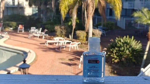 Une petite bouteille de désinfectant pour les mains est installée devant un palmier et une piscine.