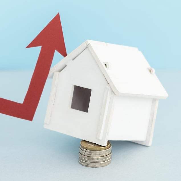 Une petite maison en bois déposée sur des pièces de monnaie. Un flèche rouge qui pinte vers le haut est appuyé sur la maison.