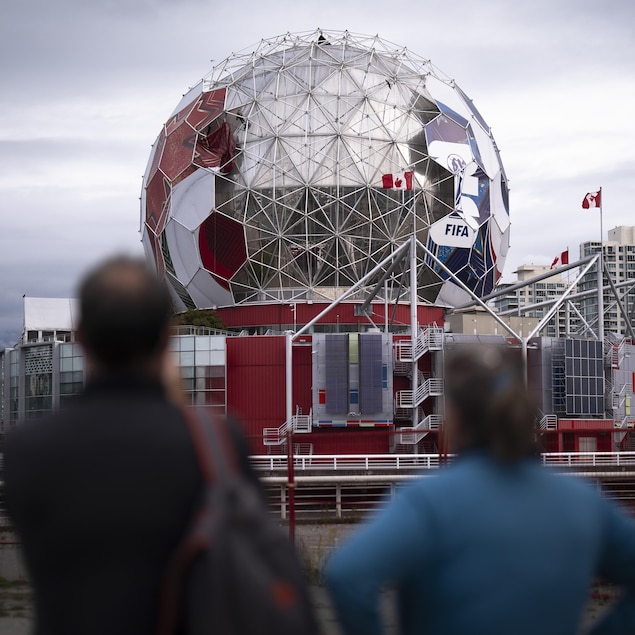 Deux personnes observent des travailleurs qui enlèvenet les panneaux du dôme de Science World à Vancouver.