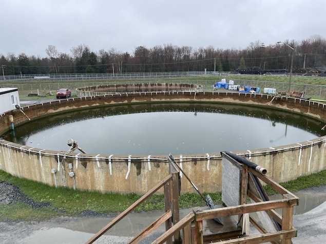 Un bassin de rétention d'eau qui ressemble à une immense piscine hors terre avec de l'eau verte dedans.