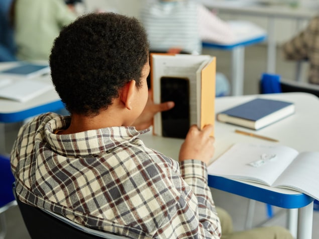 Un élève qui cache un téléphone cellulaire derrière un livre pendant qu'il est en classe à l'école.