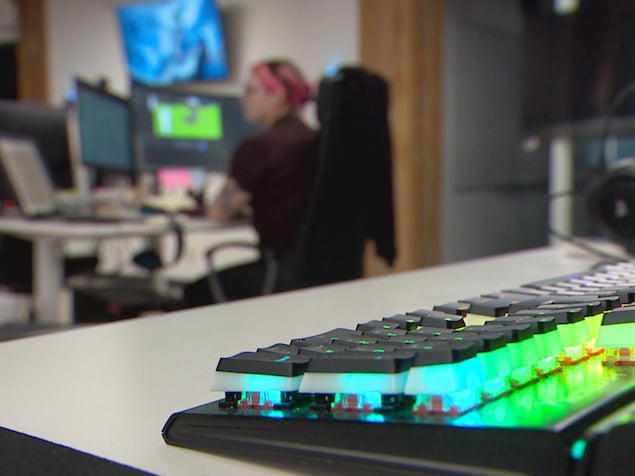 Un clavier s'illumine de plein de couleurs alors qu'une femme travaille à un ordinateur en arrière plan  