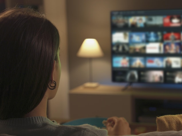 Une femme assise dans un salon qui regarde une télévision où l'on peut voir une sélection de contenus dans une plateforme de diffusion en continu.