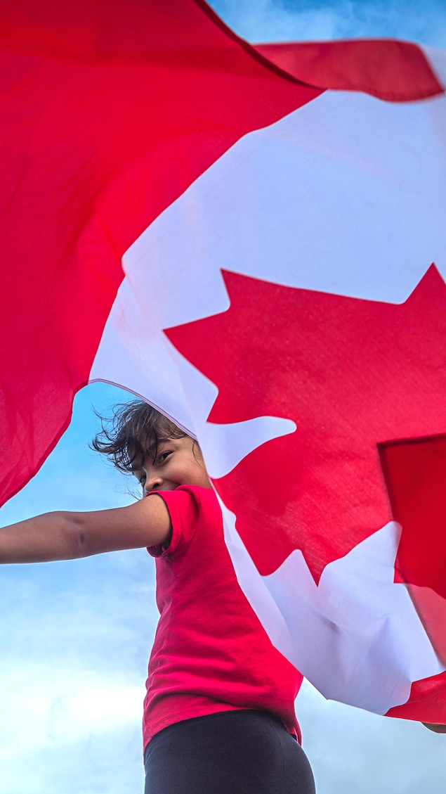 Un jeune garçon qui fait flotter un drapeau du Canada derrière lui.