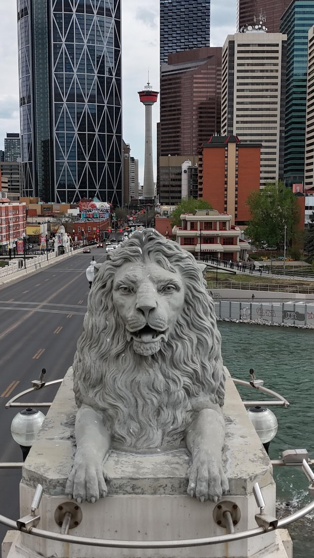 En avant plan une statue d'un lion en ciment avec la rivière et le centre-ville en arrière plan. 14 mai 2026.