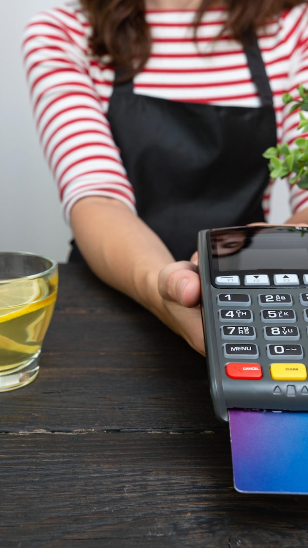 Une employée de café tend un terminal de paiement.