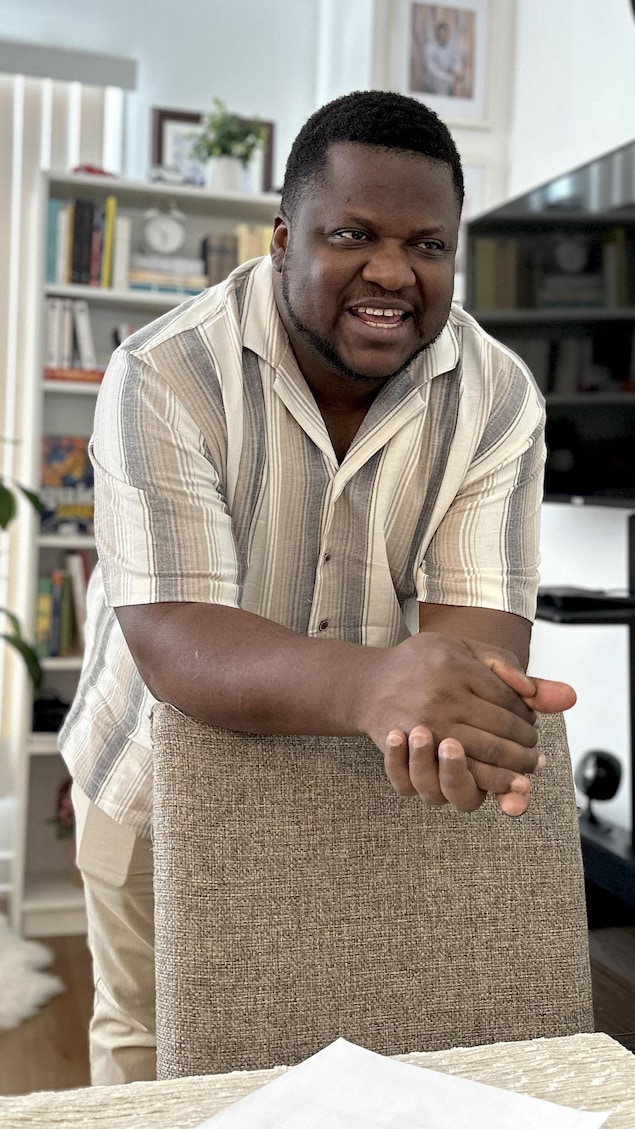 Un homme souriant appuyé sur le dos d'une chaise.