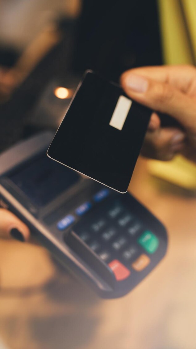 Une main tient une carte de crédit au-dessus d'un terminal de paiement.