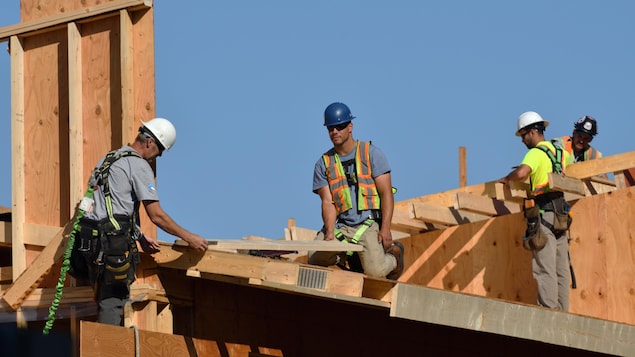 Quatre travailleurs de la construction travaillent sur un toit en été.