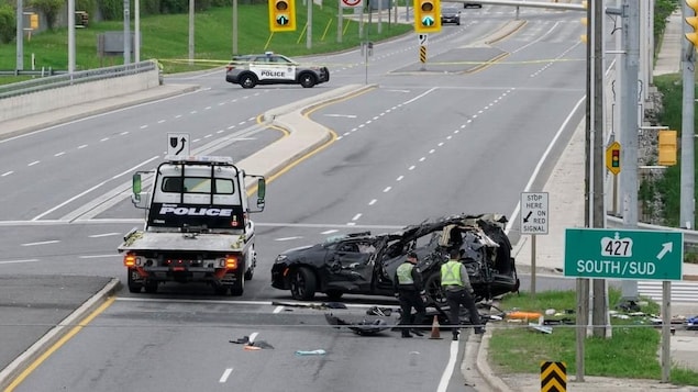 Une zone délimitée par un ruban adhésif montre une voiture endommagée et des véhicules de police garés à côté.