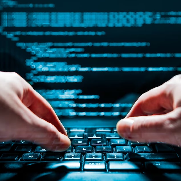 Des mains sur un clavier d'ordinateur. L'écran montre une série de codes.