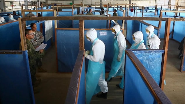 Des gens marchent en habits de protection contre un virus.