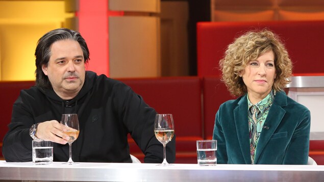 Un homme, qui porte un blouson noir, et une femme, qui porte un veston vert émeraude.