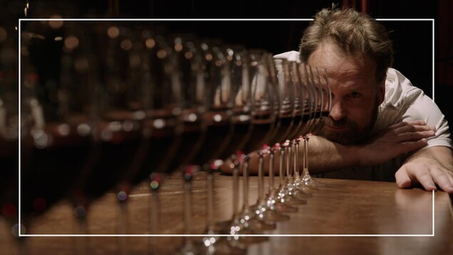 Il regarde devant lui une série de verres de vin rouge. 
