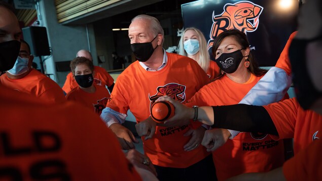 B.C. Premier John Horgan, centre, and Tk’emlúps te Secwépemc Kúkpi7 (Chief) Rosanne Casimir, right, gather together with others after the B.C. Lions CFL football team announced they would recognize the first National Day for Truth and Reconciliation on Sept. 30 at their Sept. 24 game against Saskatchewan, in Vancouver, on Thursday, September 16, 2021. Orange t-shirts with an Indigenous B.C. Lions logo by Kwakwaka'wakw-Tlingit artist Corrine Hunt will be handed out to 10,000 people at the game a