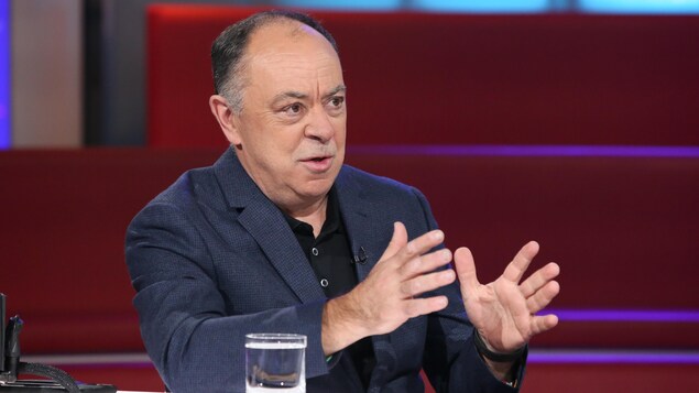 Un homme qui porte un chandail noir et un veston bleu.