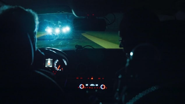 Deux personnes sont dans une voiture, la nuit, et des voitures arrivent en sens inverse, les phares allumés.