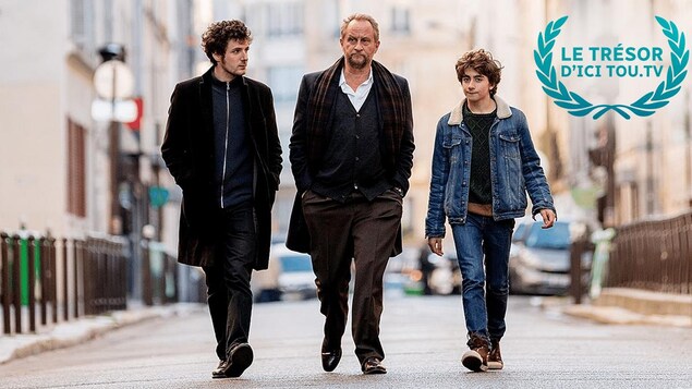 Un homme (Benoît Poelvoorde) marche dans la rue, entouré de deux jeunes hommes.